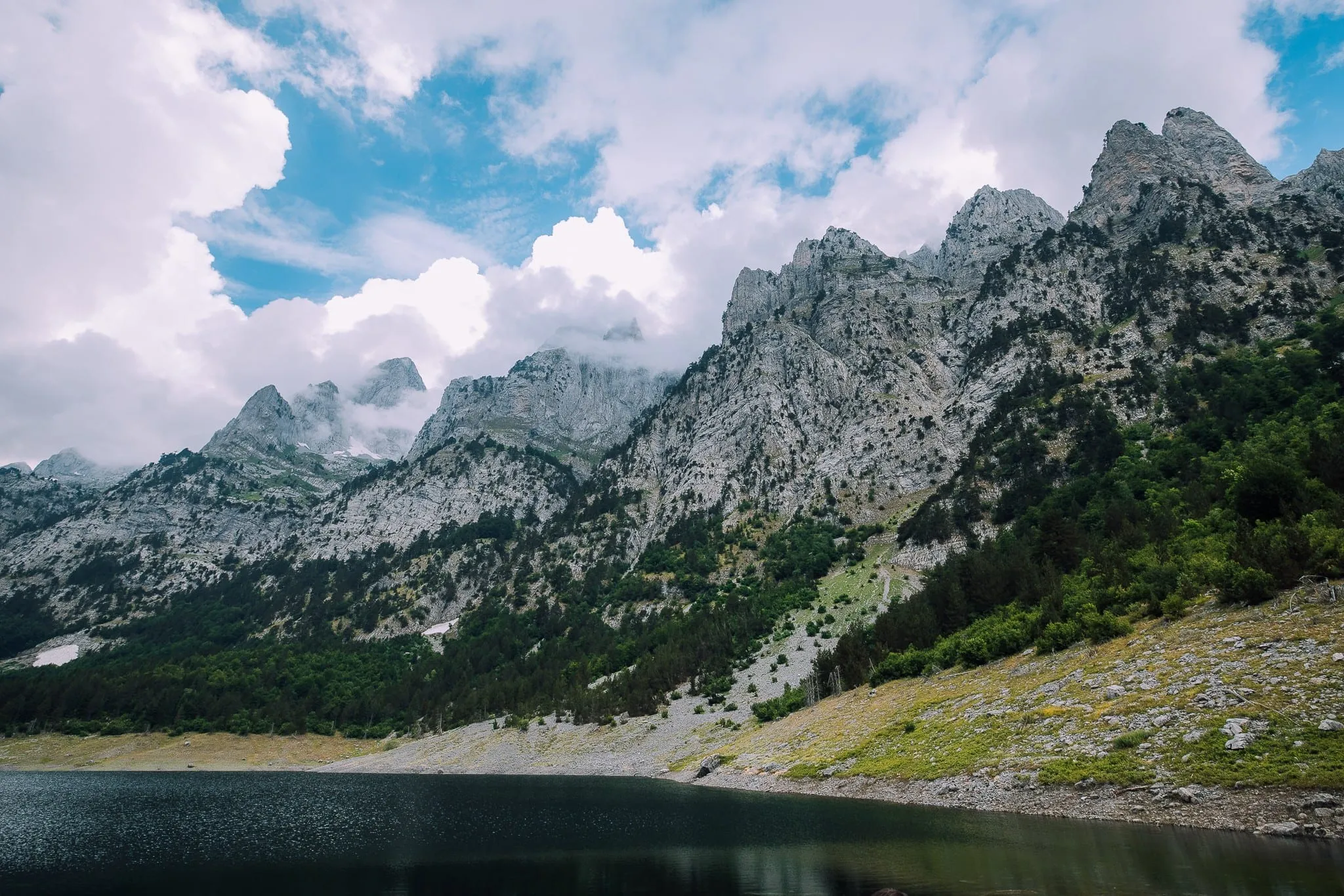 Ein dunkler Bergsee unter zerklüfteten, wolkenverhangenen Kalksteingipfeln im Nationalpark Theth